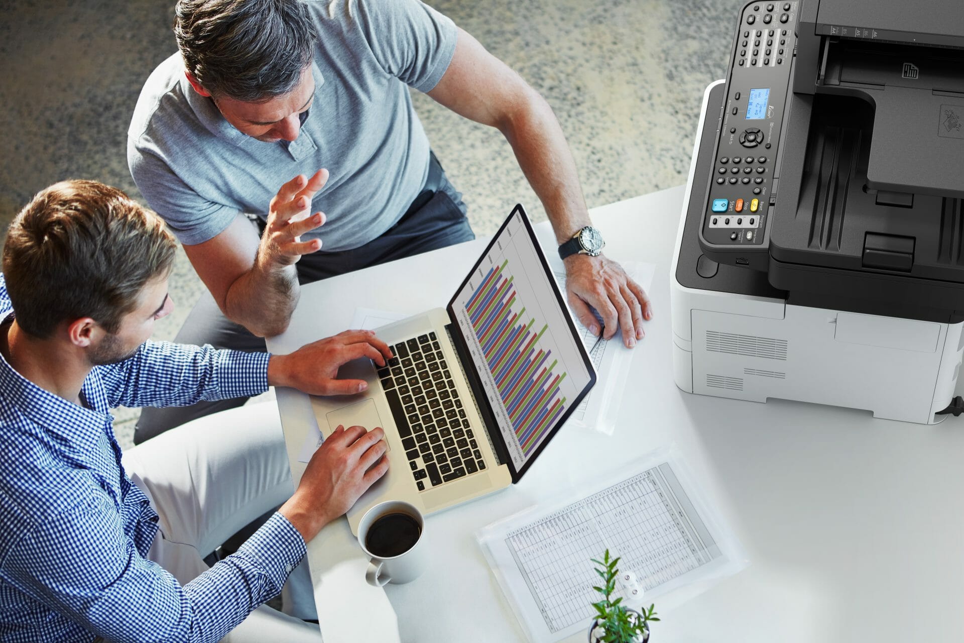 Two people working at a laptop beside a Kyocera multifunction printer on a shared desk