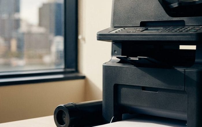Desktop multifunction printer on an oak bench in a Sydney office with a toner cartridge and a stack of A4 paper beside it