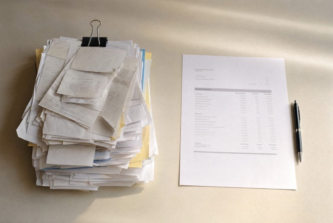 A thick untidy pile of paper invoices and statements on a desk