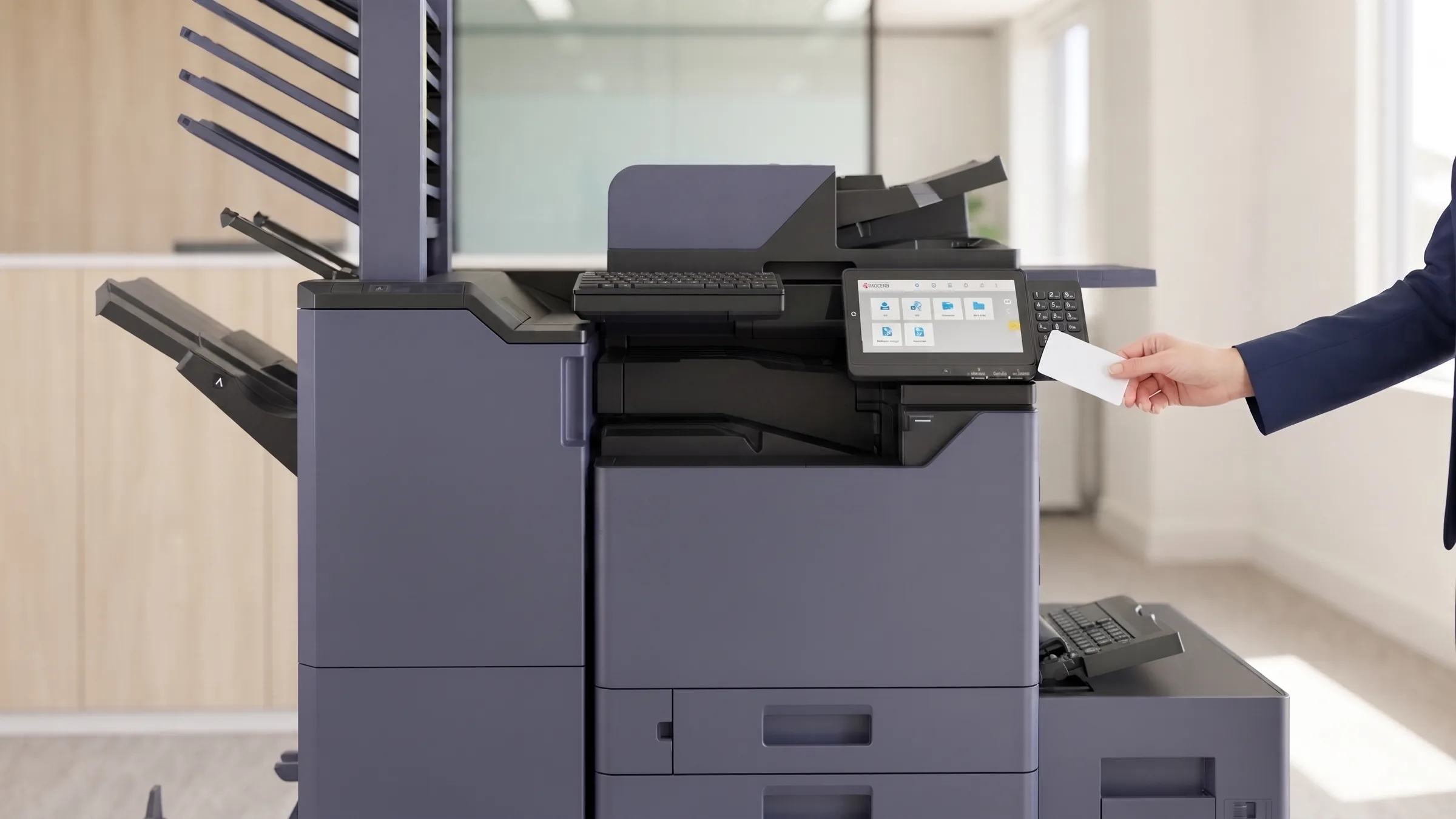An accountant holding an access card to the control panel of a leased Kyocera multifunction printer to release a held print job