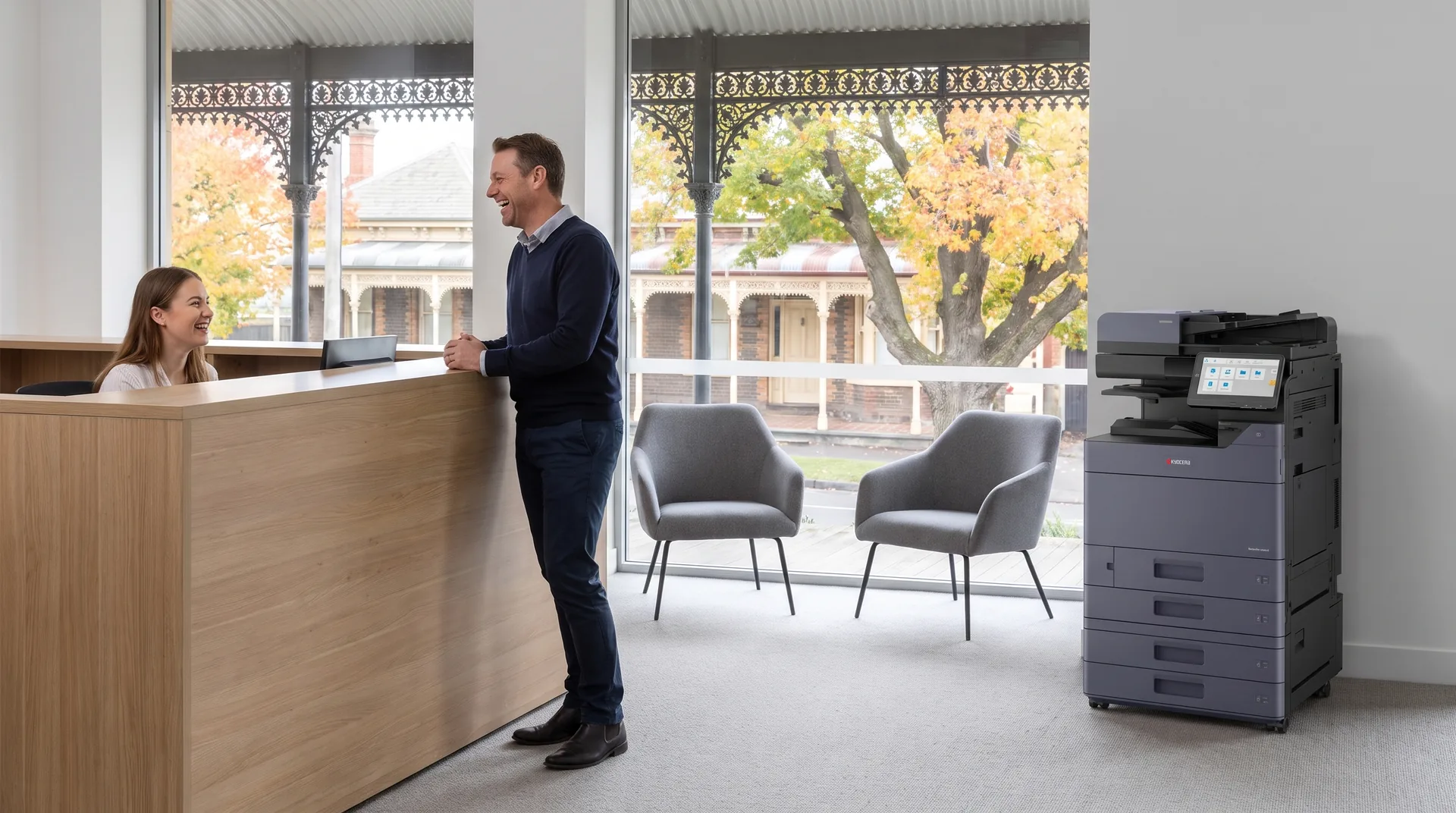 Receptionist and client laughing in a Ballarat reception area with a Kyocera photocopier on lease and a heritage verandah street outside