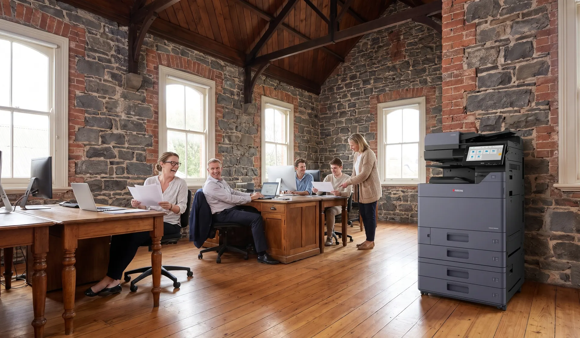 Smiling team working beside a Kyocera multifunction printer in an open plan Ballarat office inside a restored bluestone building